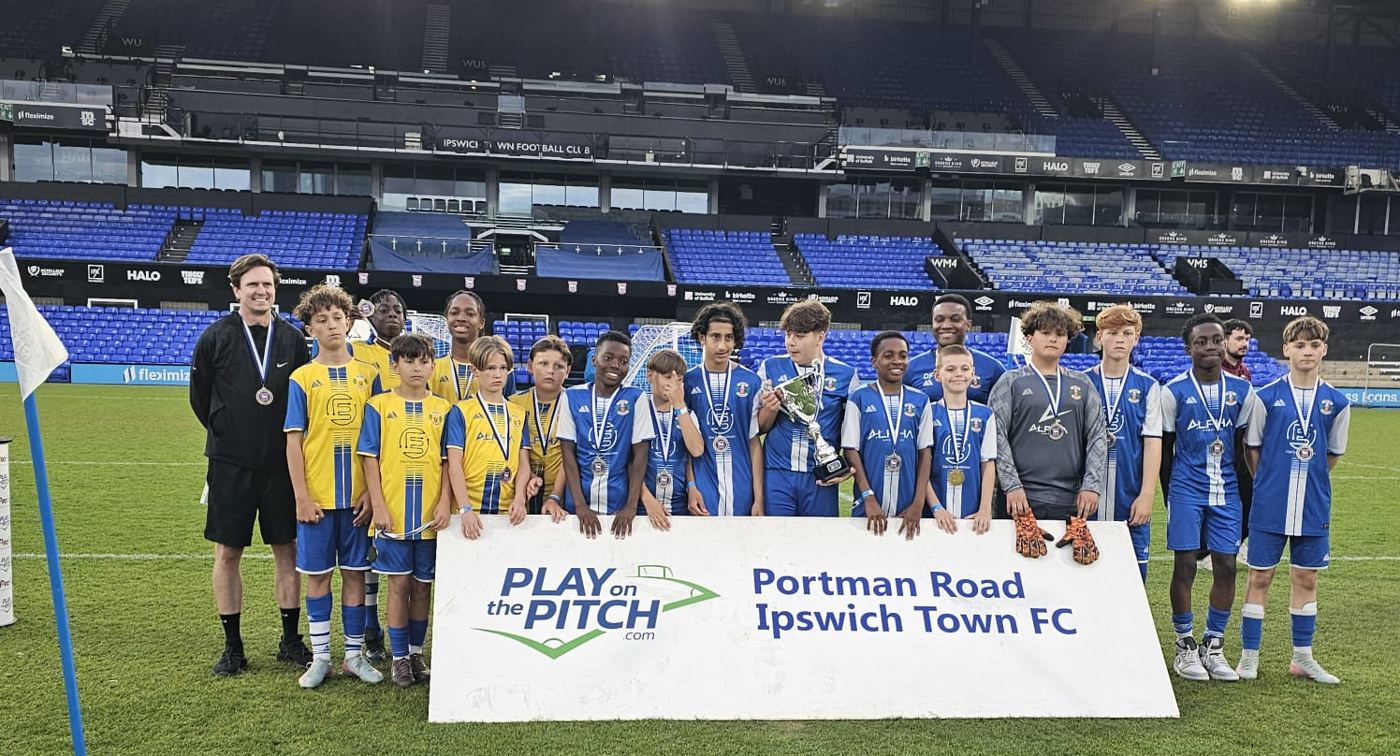 A Grays Athletic youth team with medals and a trophy on the pitch at Portman Road, Ipswich Town's stadium